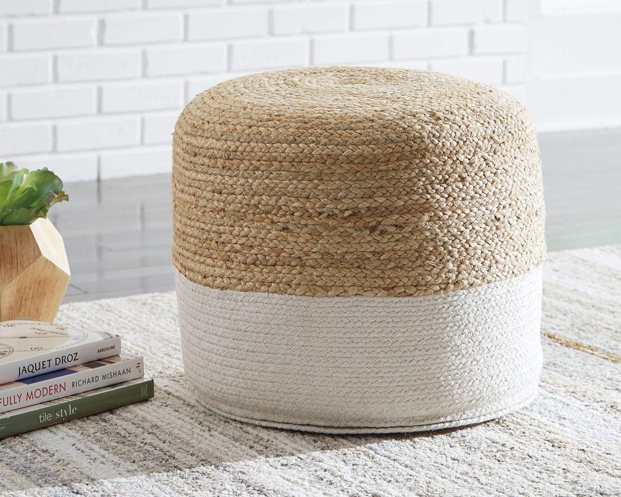 Round pouf with woven tan top and light gray base, soft braided fabric texture.