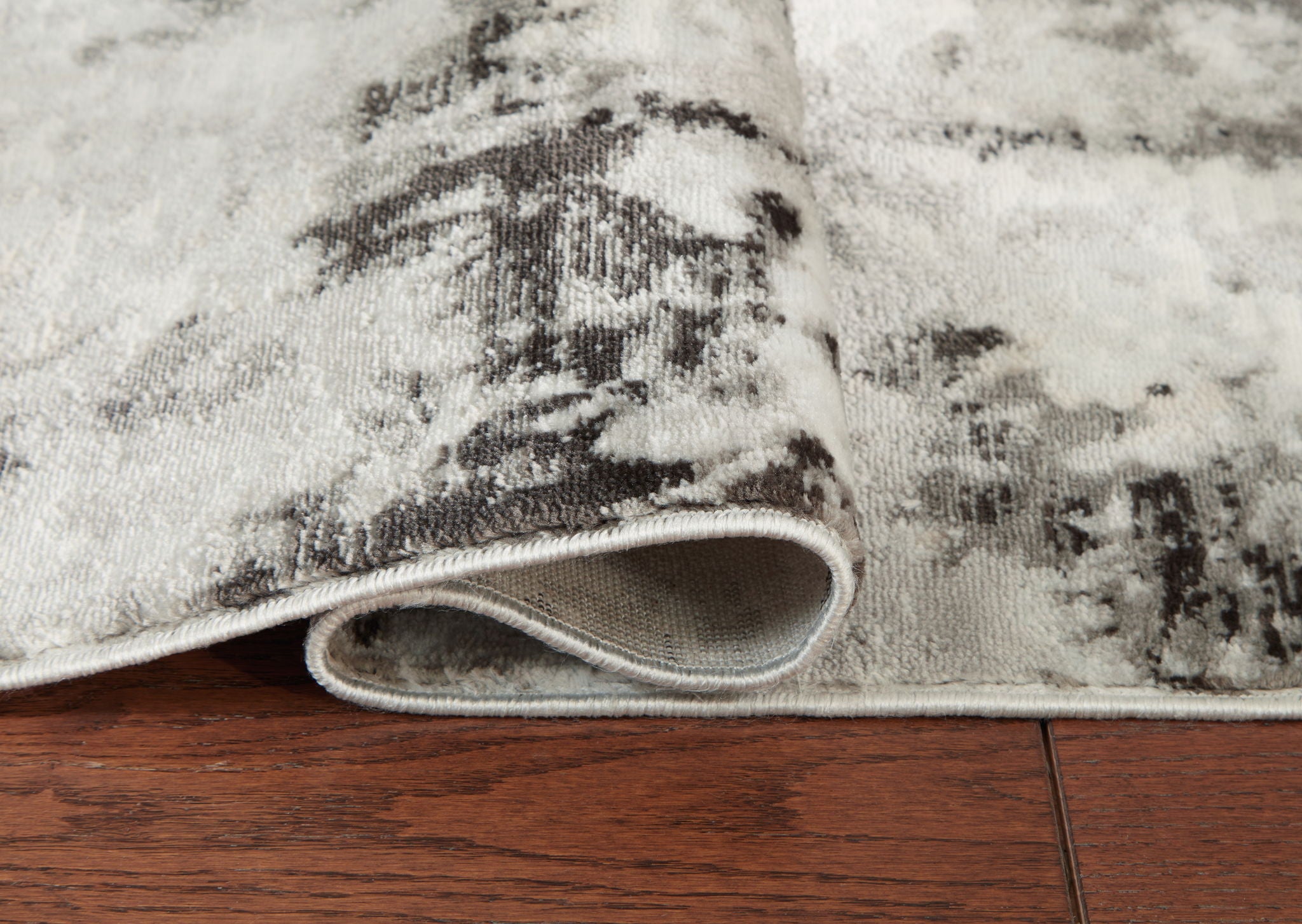Area rug rolled edge, showing gray underside and black-and-gray distressed pattern
