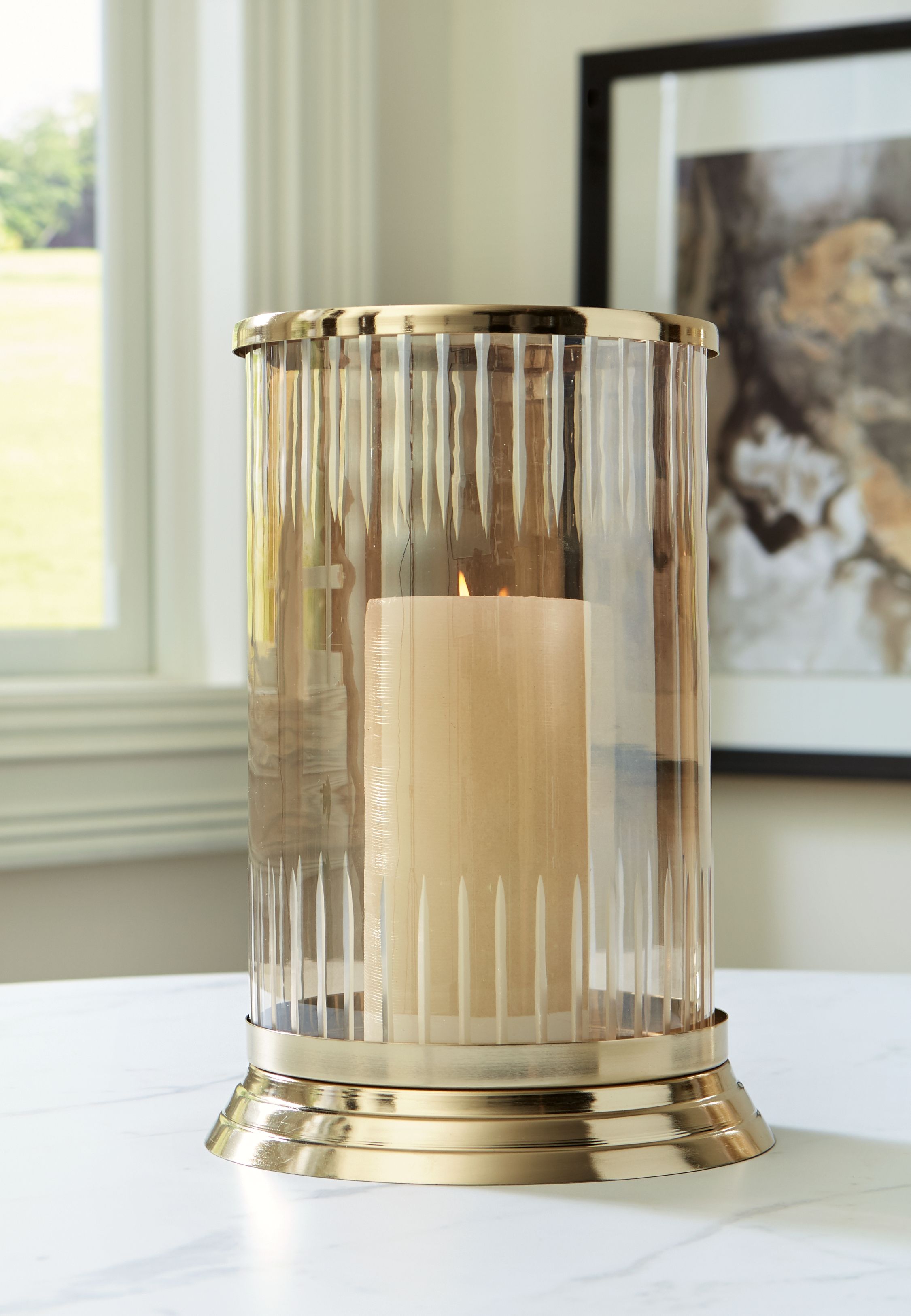 Aavinson glass candle holder with gold base on table, lit candle inside