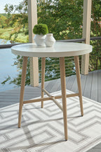 Beige round bar table on outdoor patio with shelf and tapered legs