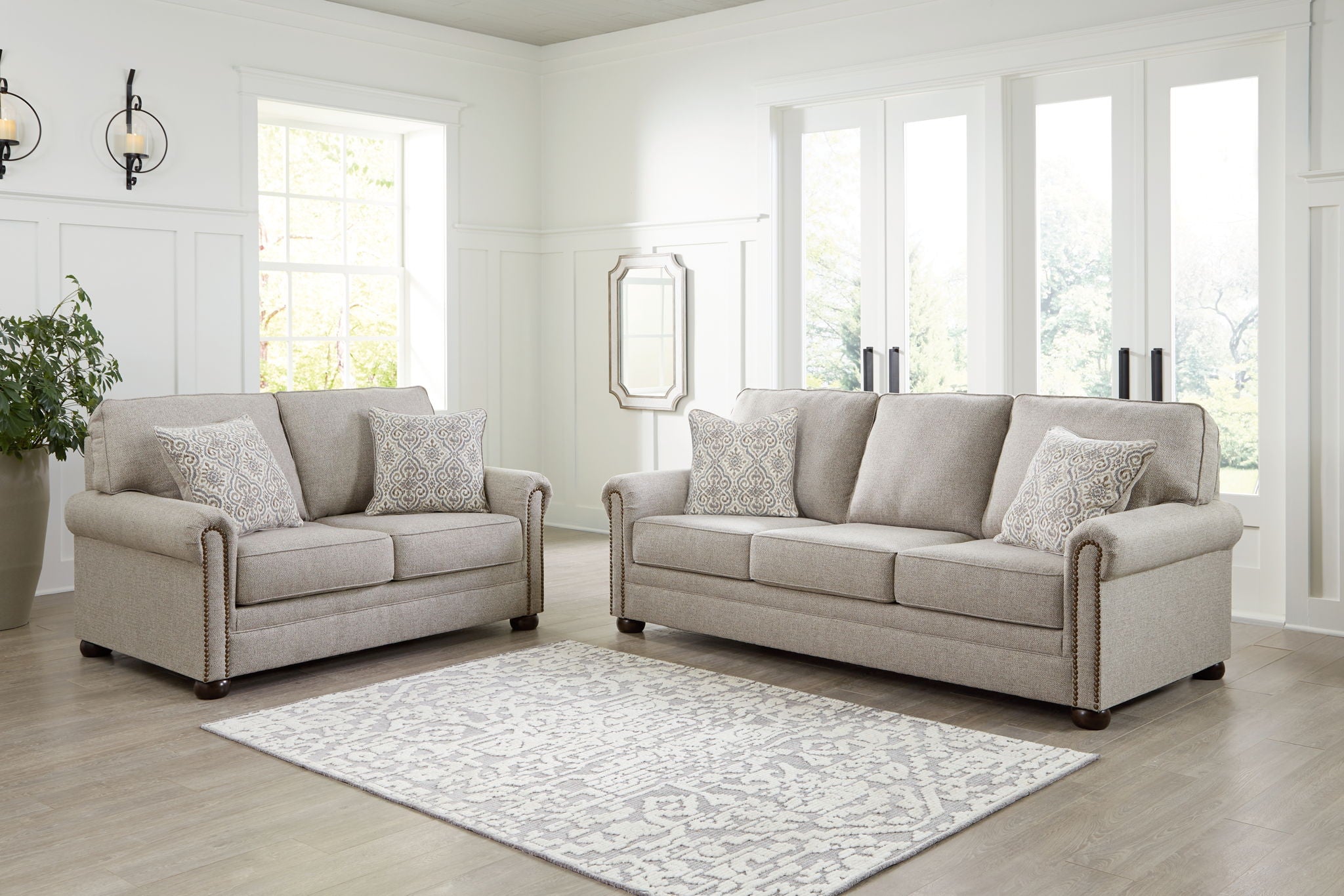 Light gray sofa set with two pieces, decorative arm trim, and patterned throw pillows.