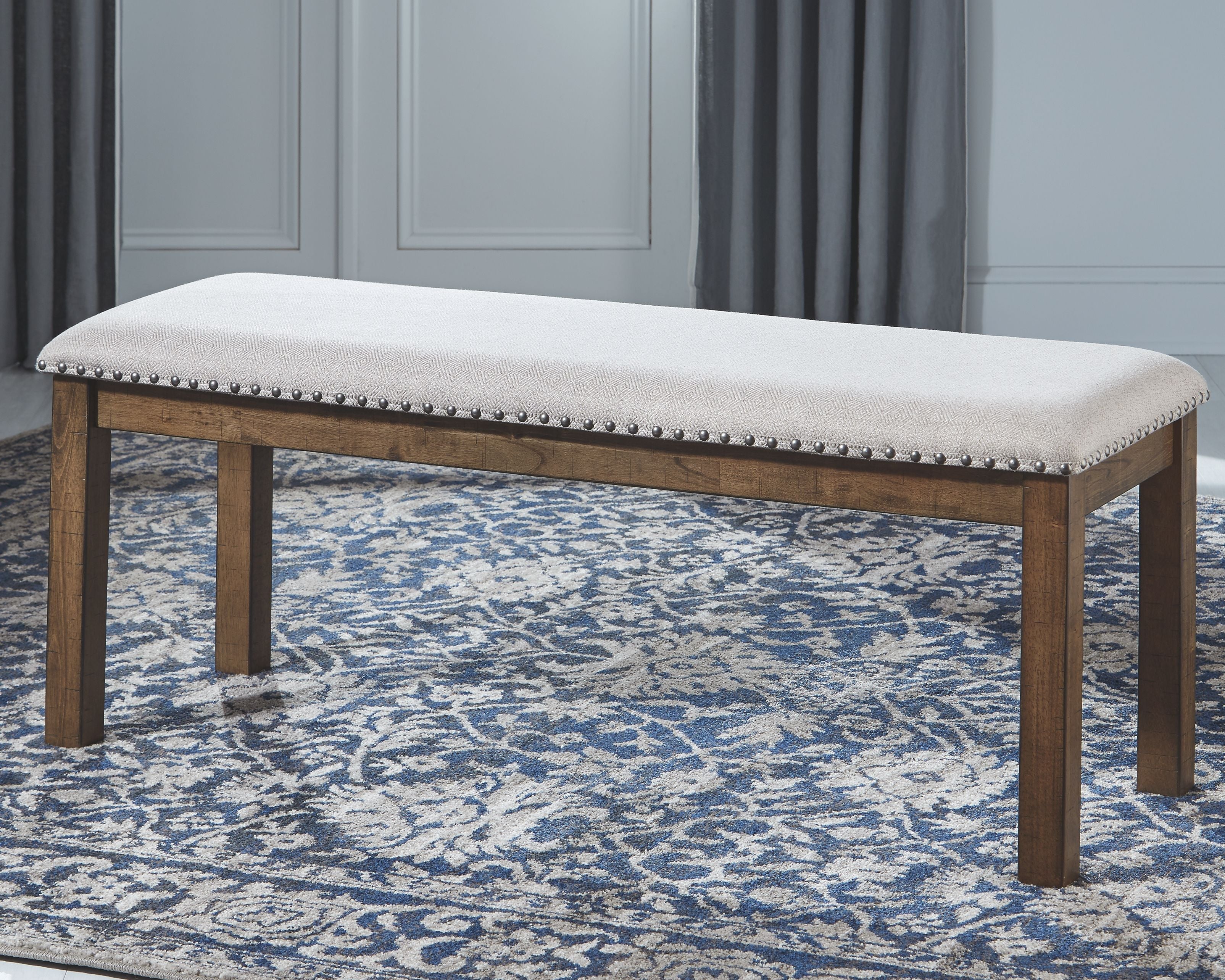 Beige upholstered bench with tufted seat, nailhead trim, and dark wood frame