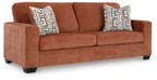 Burnt orange-brown upholstered sofa with two decorative geometric throw pillows.