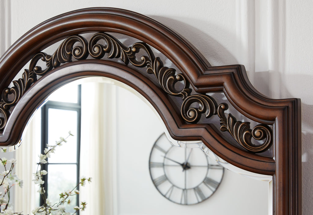 Ornately carved arched mirror frame on dark brown dresser
