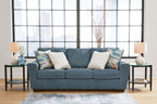 Blue fabric sofa with three seat cushions and patterned accent pillows