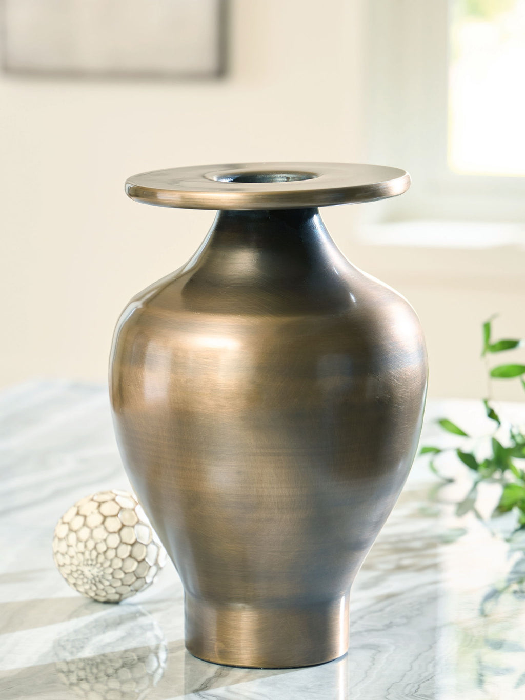 Bronze metal vase with wide circular rim, rounded body, and open top, photographed with decor.