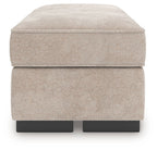 Taupe upholstered ottoman with rounded top and visible black legs