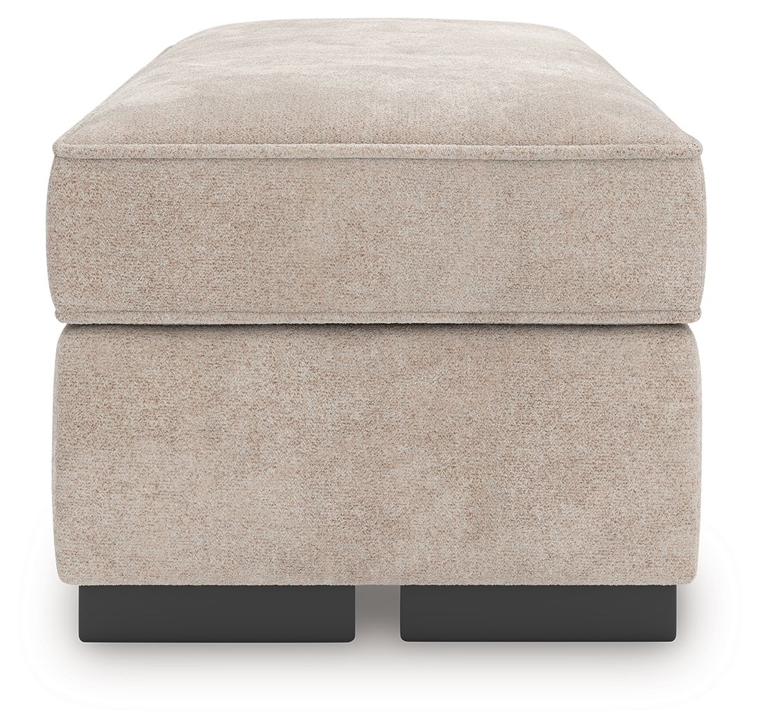 Taupe upholstered ottoman with rounded top and visible black legs