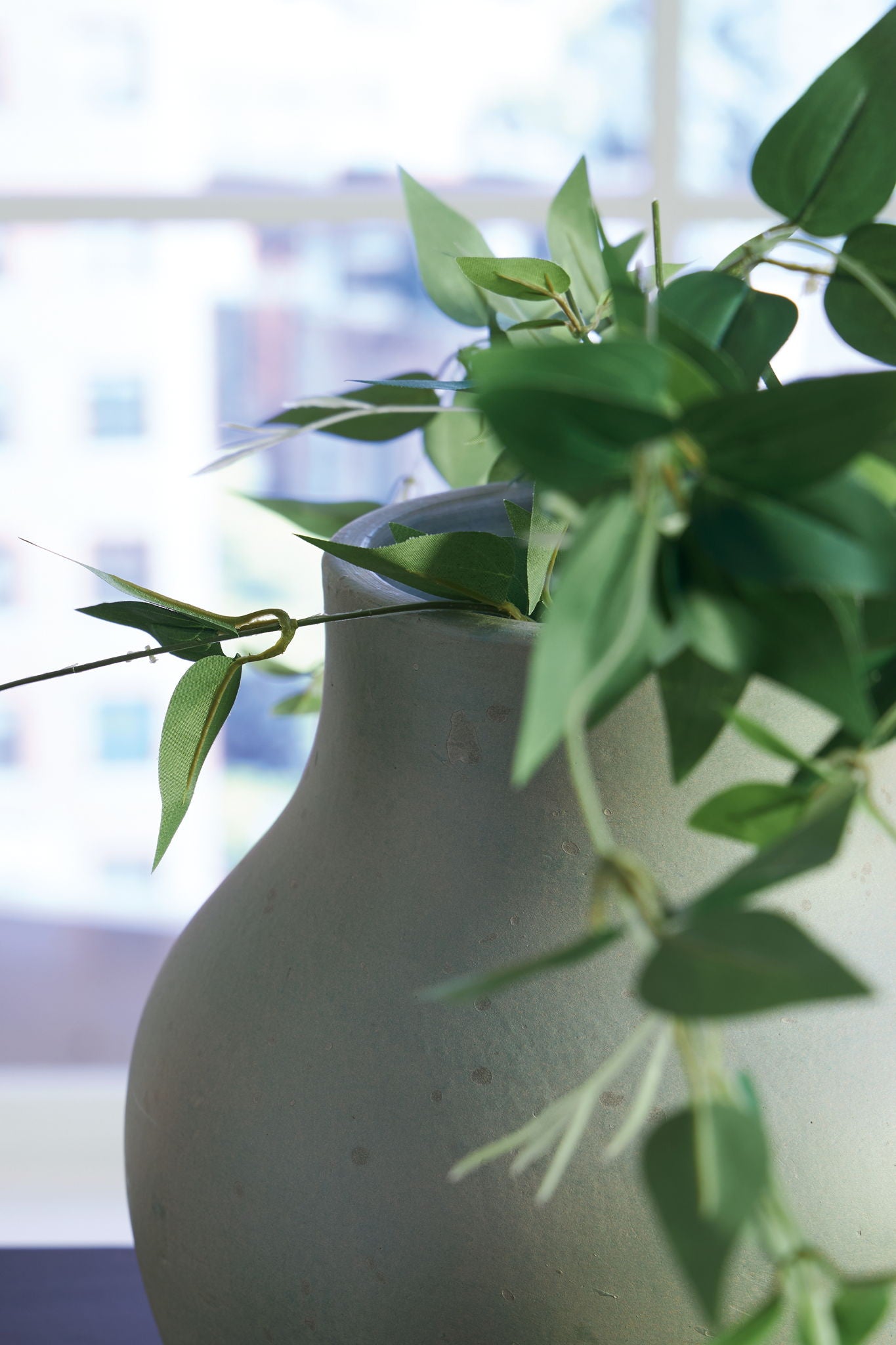 Green ceramic vase with open top and surrounding leaves