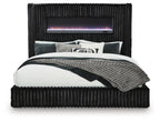 Black upholstered bed with ribbed headboard, fireplace display, and quilted coverlet