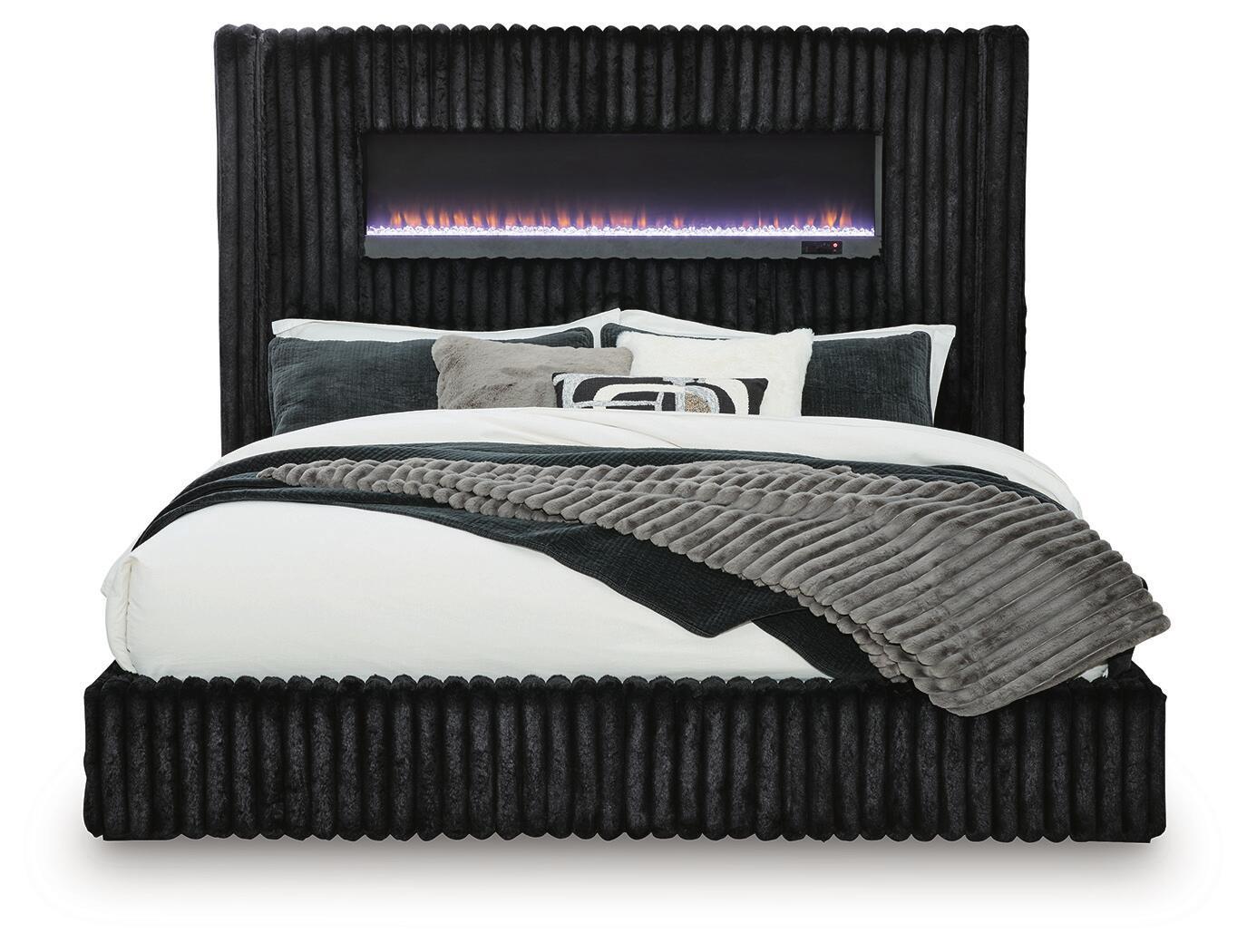 Black upholstered bed with ribbed headboard, fireplace display, and quilted coverlet