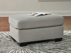 Light gray upholstered ottoman with rounded lid, ribbed upholstery, and dark legs