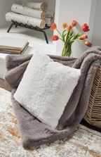 Light gray faux fur square pillow on top of a folded throw blanket.