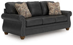 Dark gray sofa with tufted arm trim and two patterned throw pillows