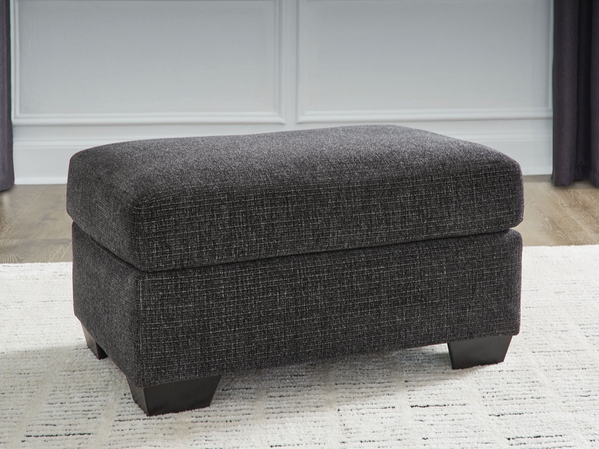 Dark gray upholstered ottoman with padded top and black block feet