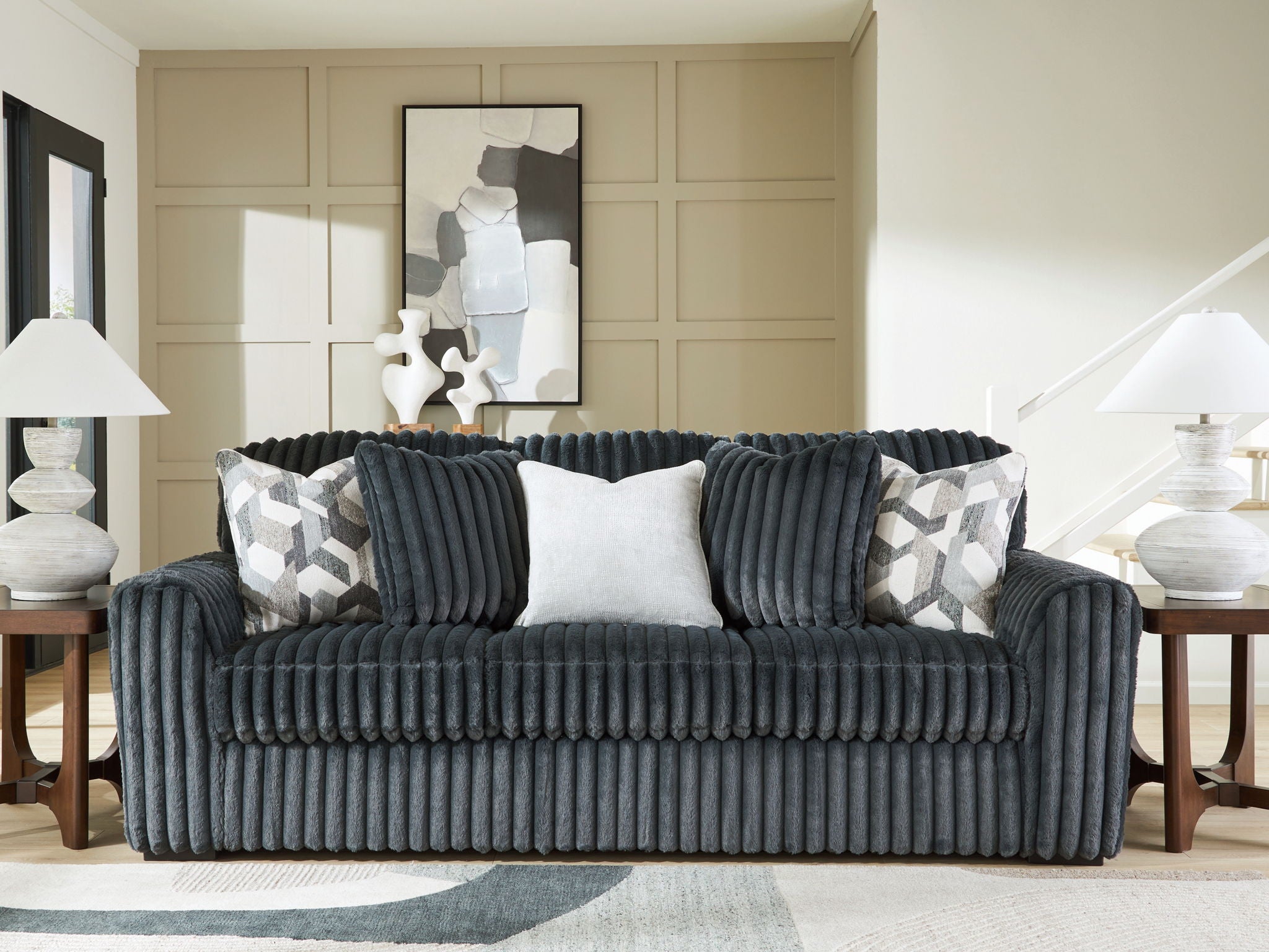 Dark gray corduroy sofa with two patterned throw pillows and a solid light center back cushion.