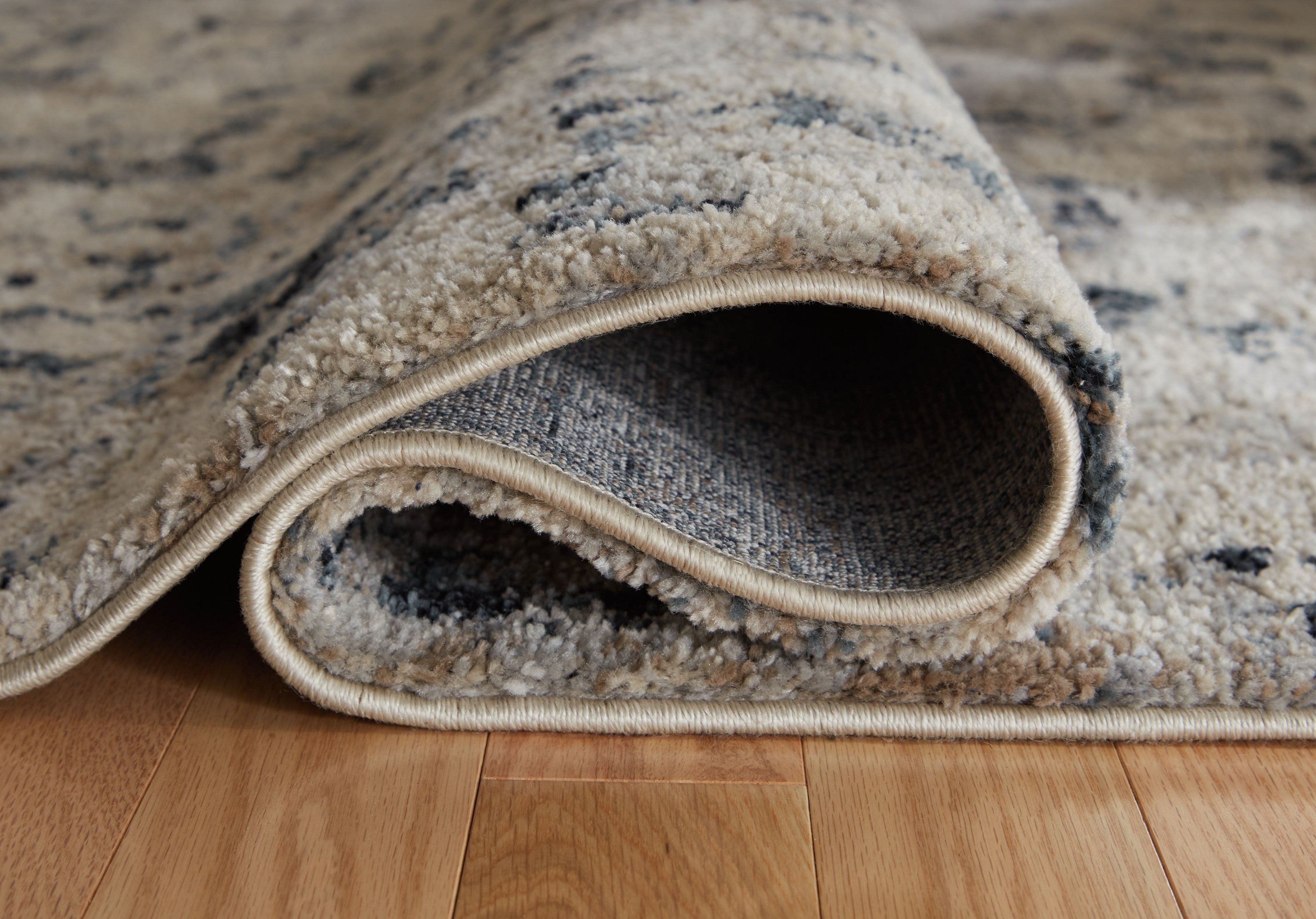 Grey and off-white area rug with textured pile and stitched border; underside shows