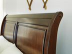 Brown sleigh bed headboard with curved wood panels and dark metal nail accents