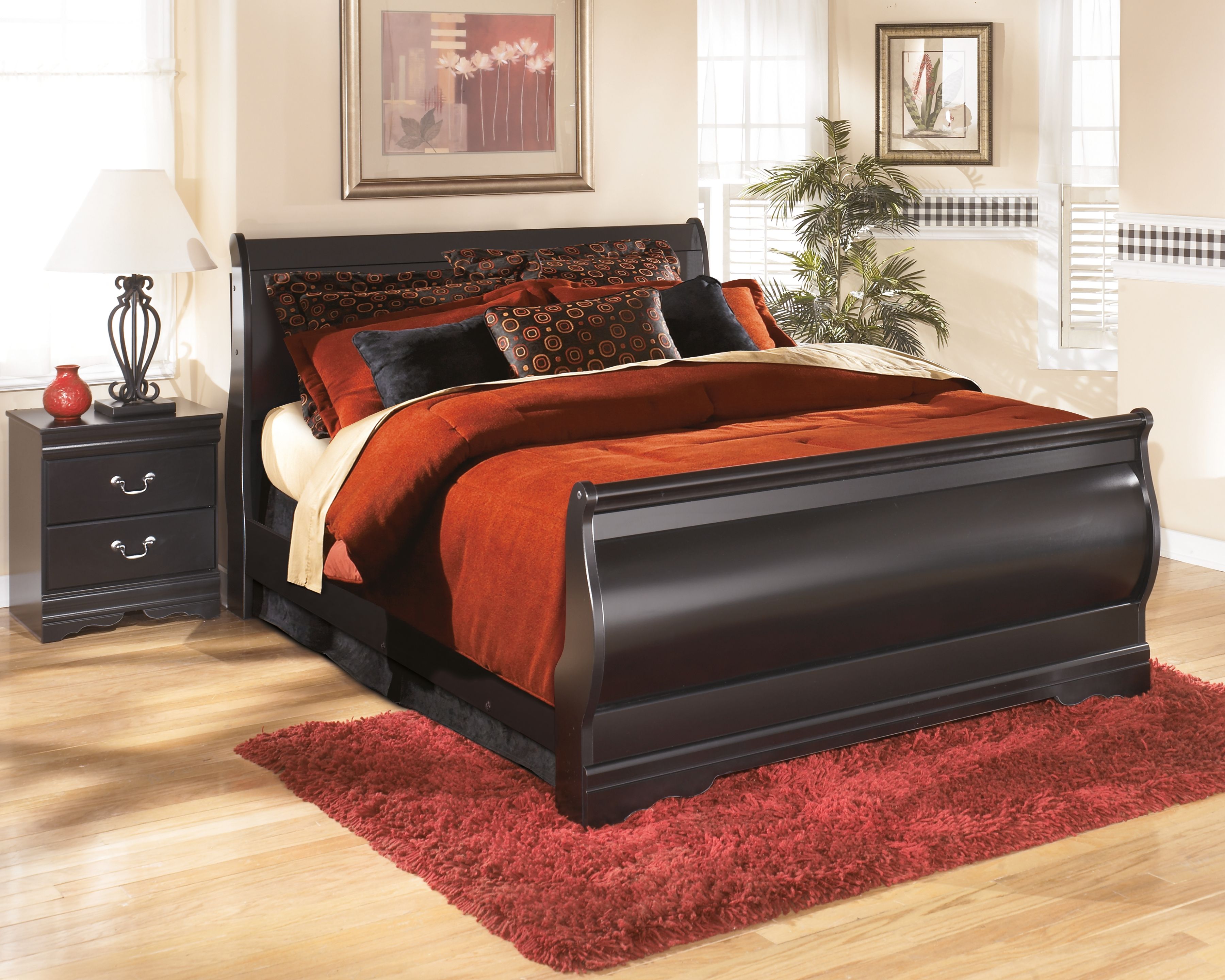 Black wooden bed frame with raised headboard, matching nightstands, and red bedding