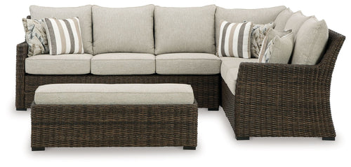 Brown wicker corner sofa with beige seat cushions, ottoman bench, striped pillows