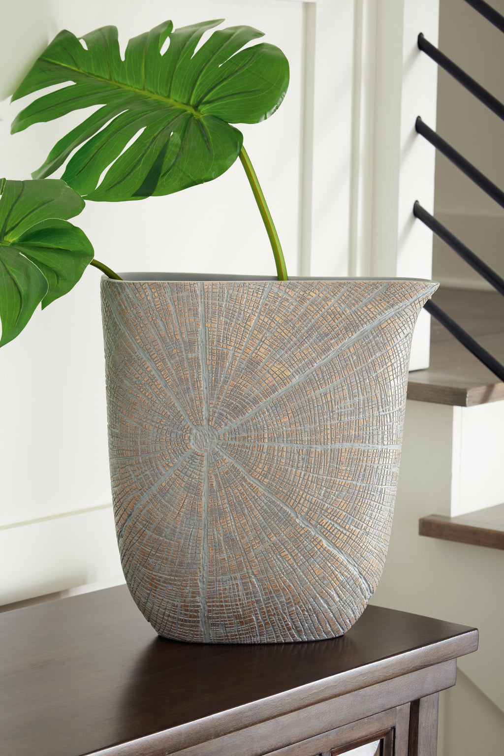 Blue-gray vase with radial mosaic pattern holding green leaves
