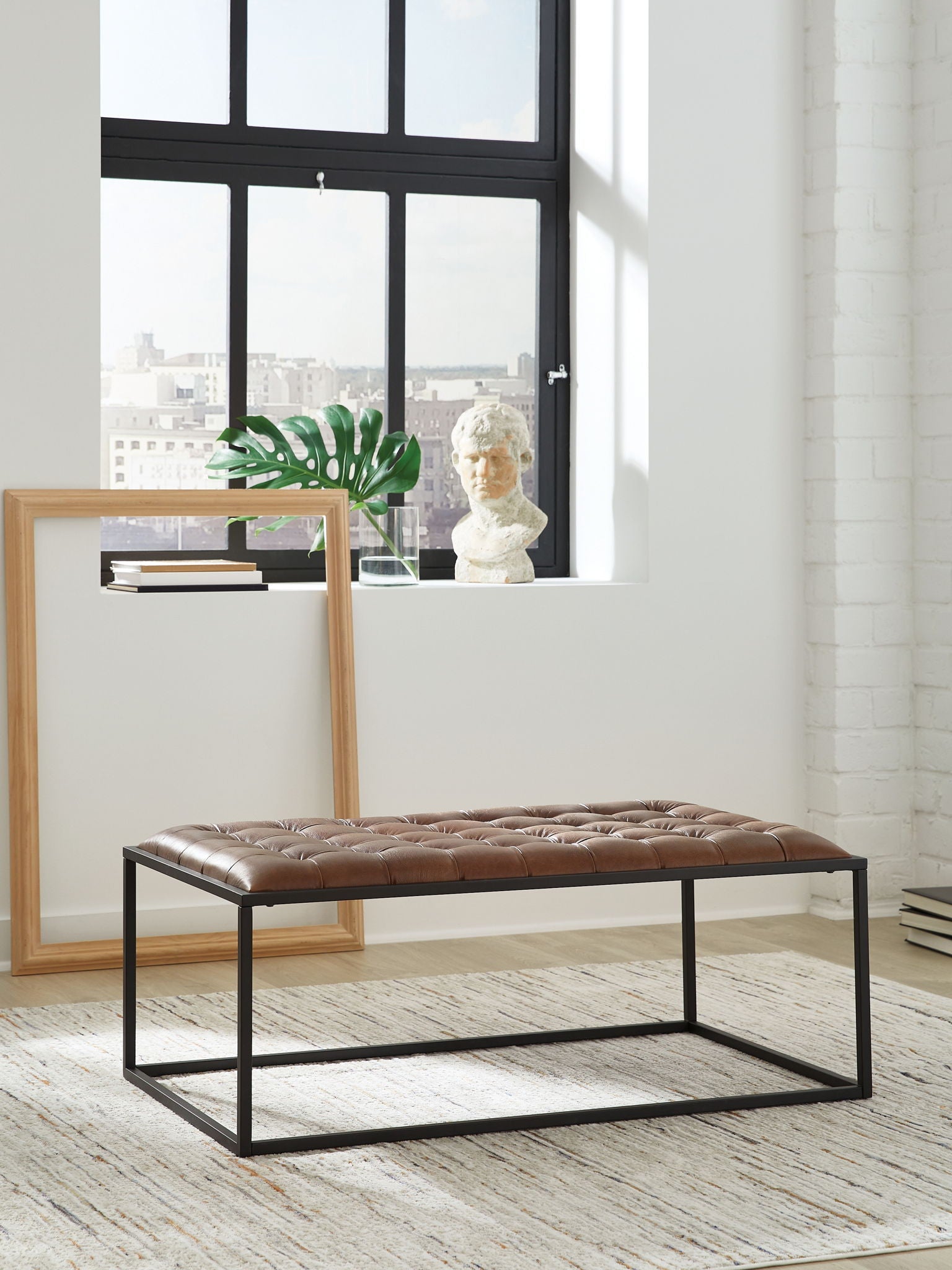 Brown leather-look tufted cocktail ottoman with black metal frame and seat