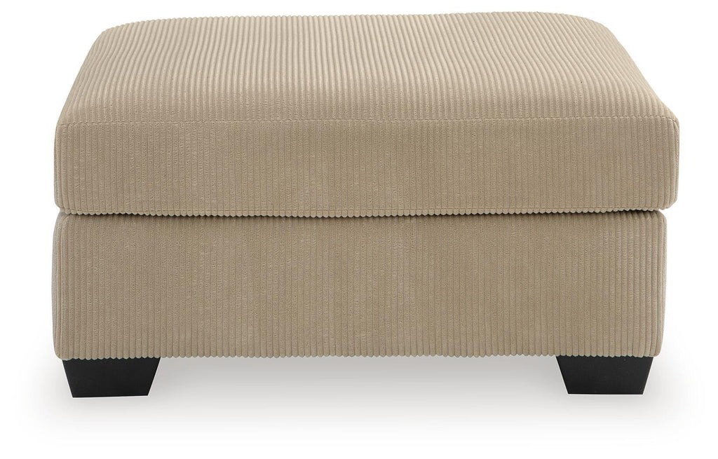 Light beige oversized ottoman with ribbed fabric, square padded top, dark legs.