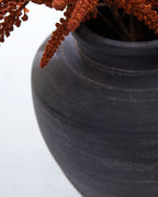 Dark blue ceramic vase with wide mouth and textured surface, with stems inside