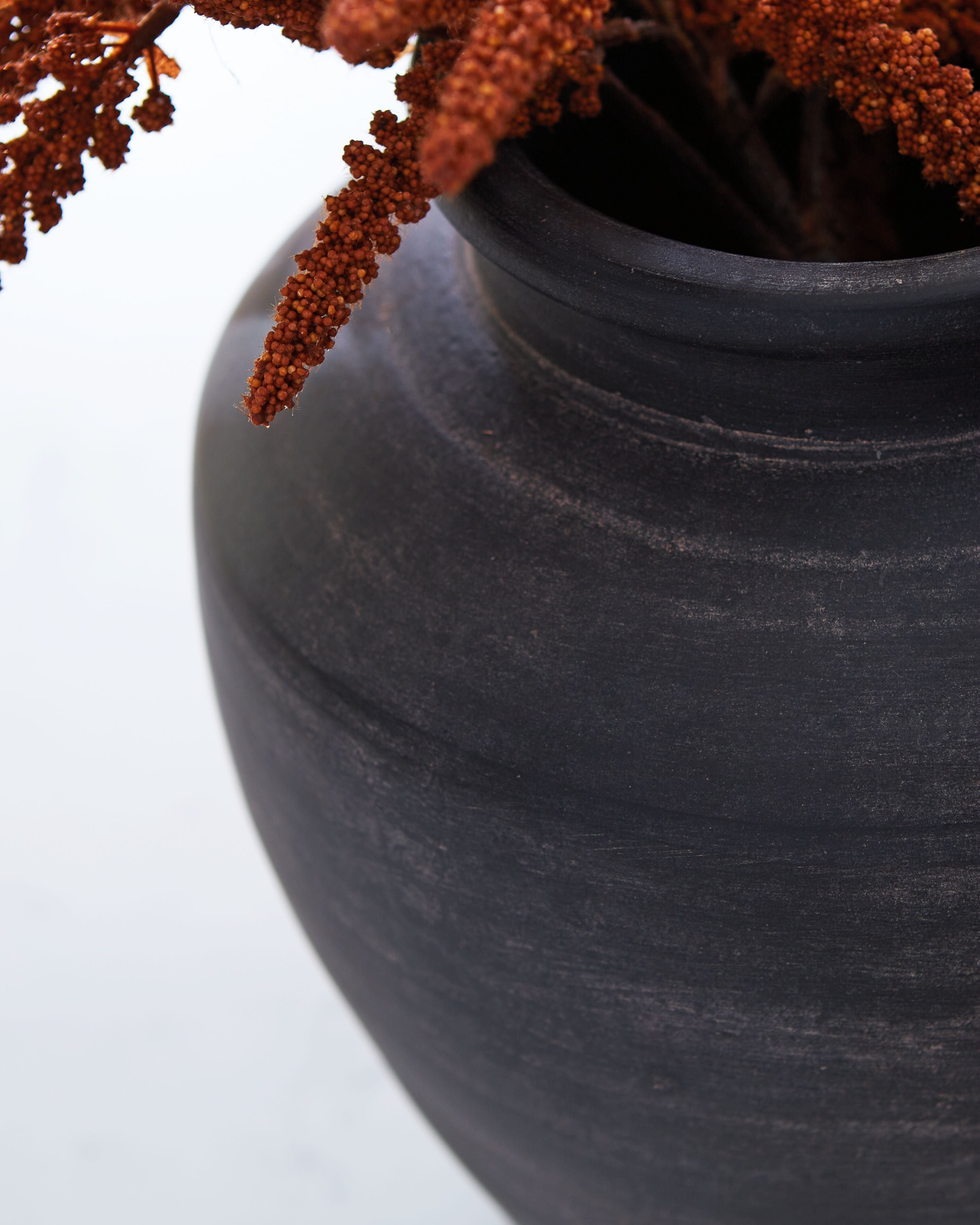 Dark blue ceramic vase with wide mouth and textured surface, with stems inside