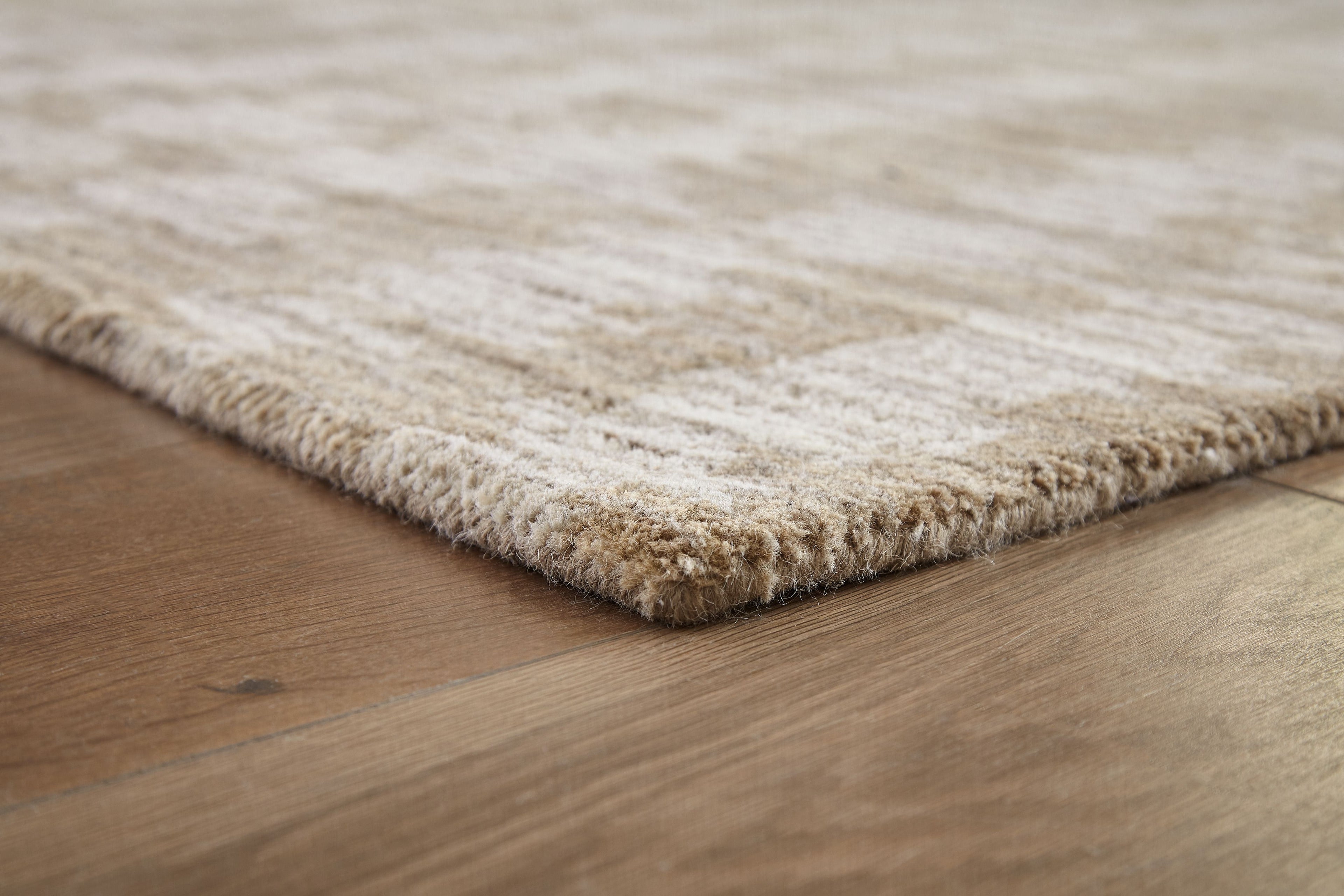 Light brown area rug corner with short fringe trim and textured flat weave