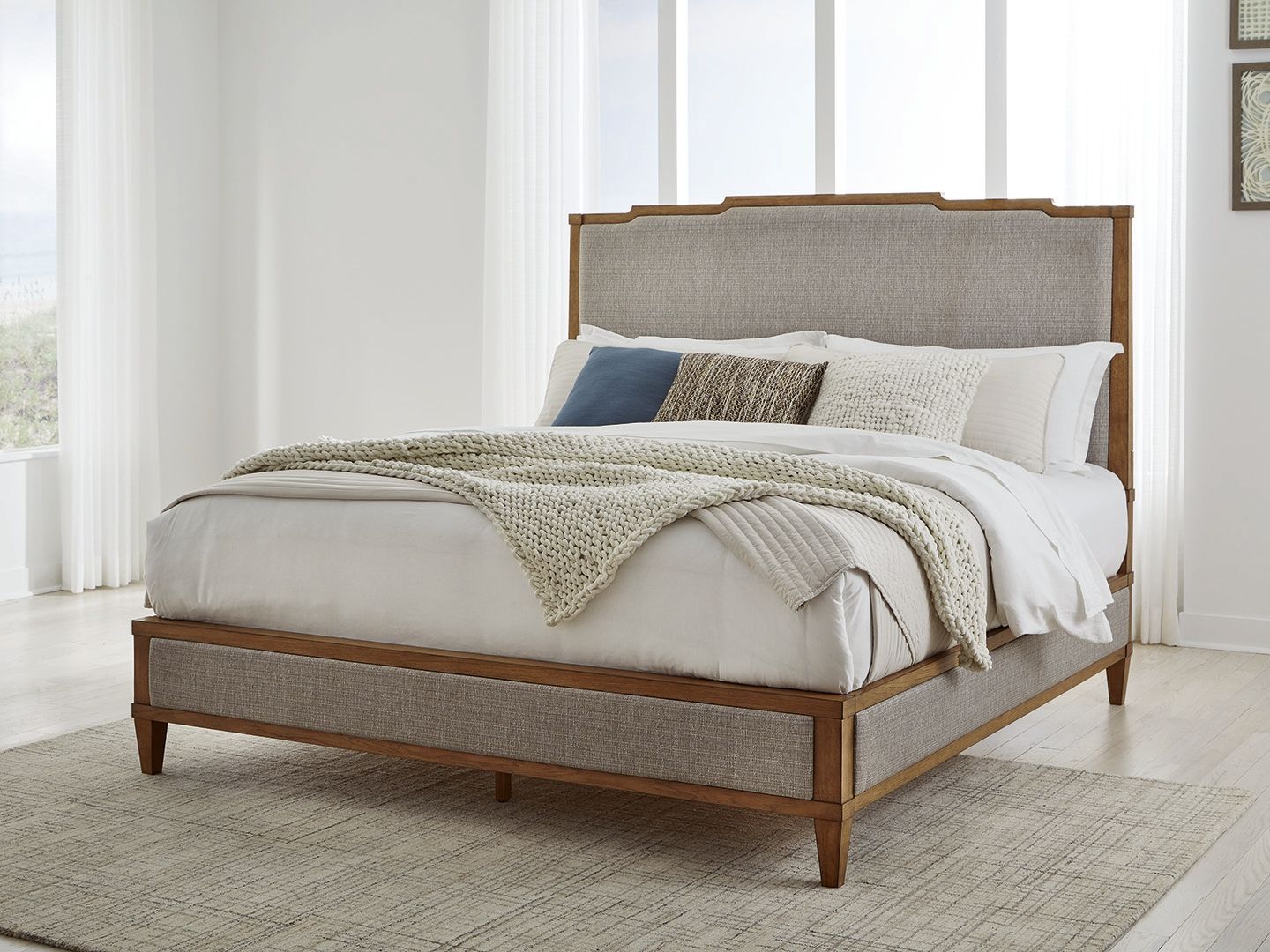 Upholstered panel bed with light gray base, wooden frame, white bedding and folded blanket