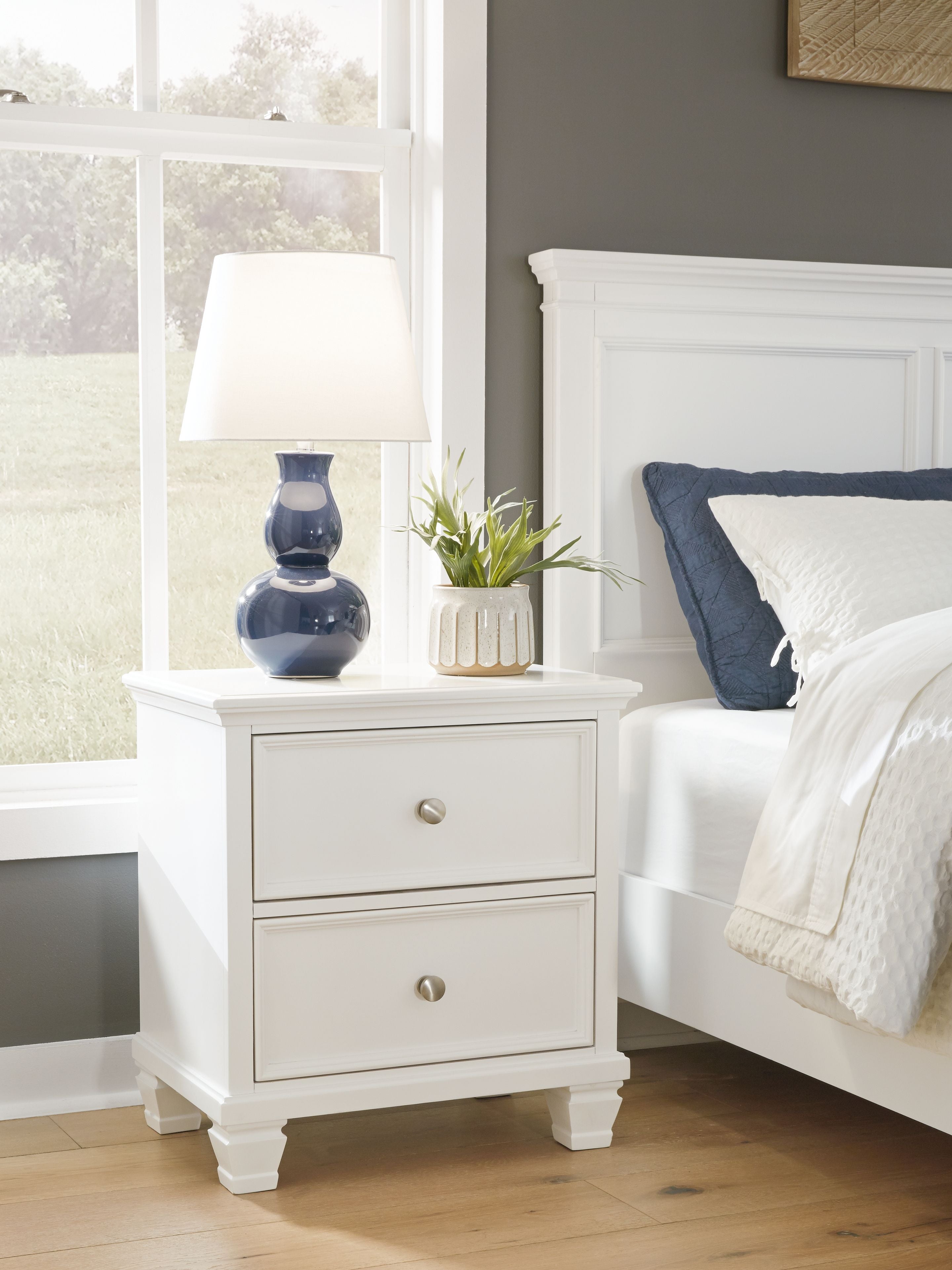 White two-drawer night stand beside a bed, with round knobs on drawers