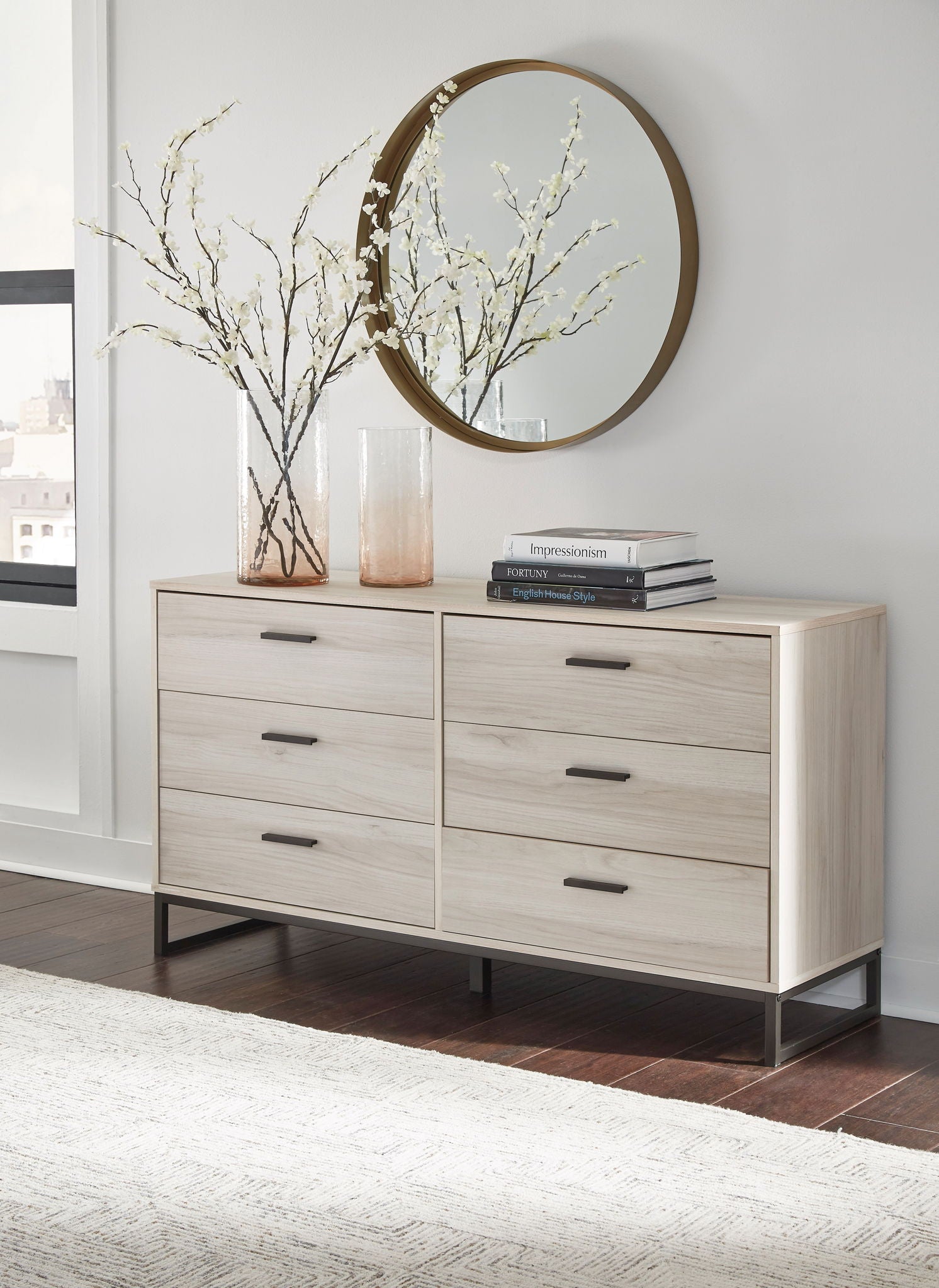 Light wood bedroom dresser with multiple drawers and round wall mirror