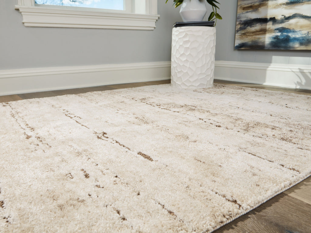 Beige area rug corner with distressed linear motifs and low pile.