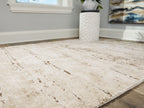 Beige area rug corner with distressed linear motifs and low pile.