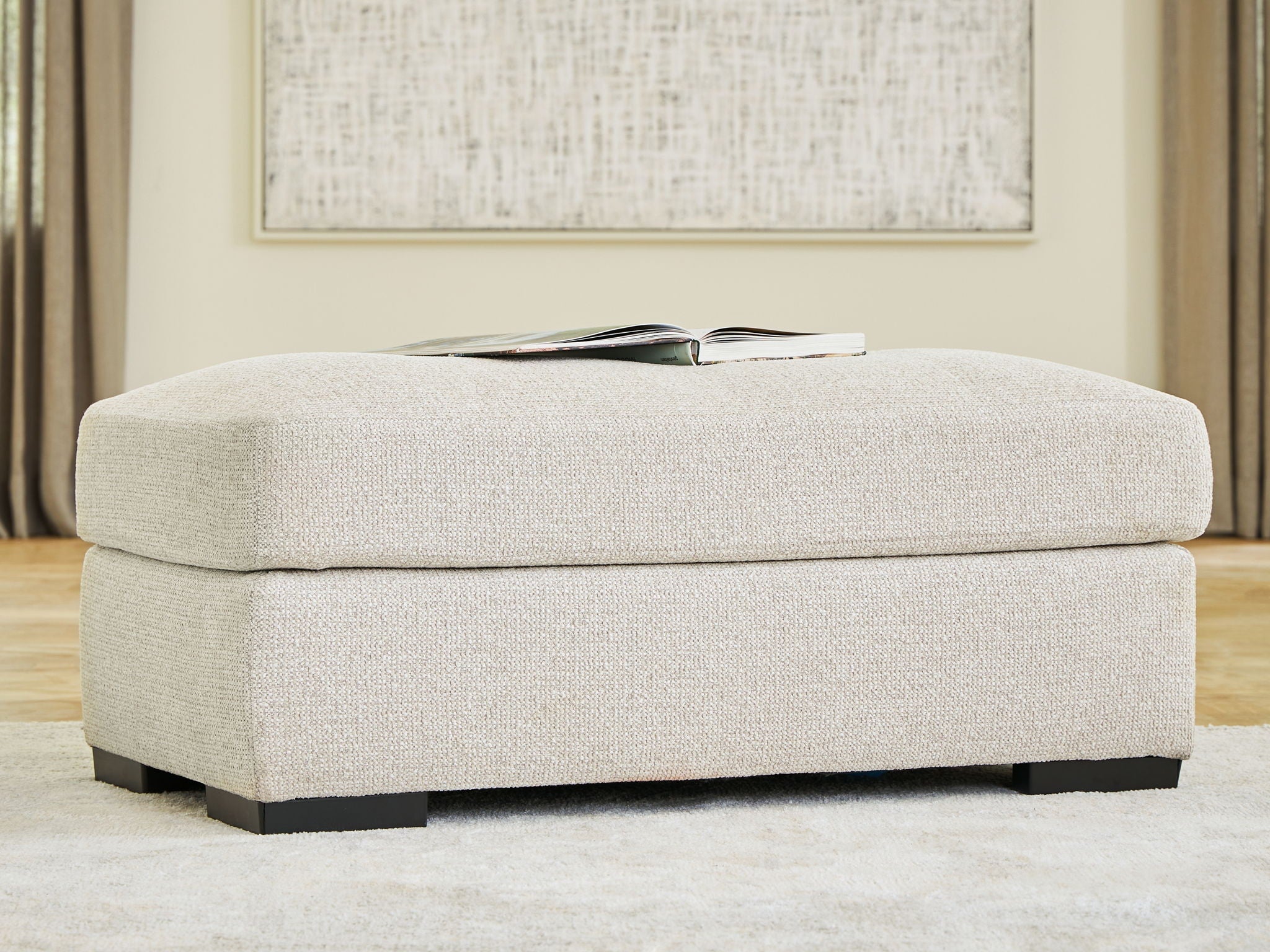 Upholstered ottoman with light beige linen fabric and low dark wood legs