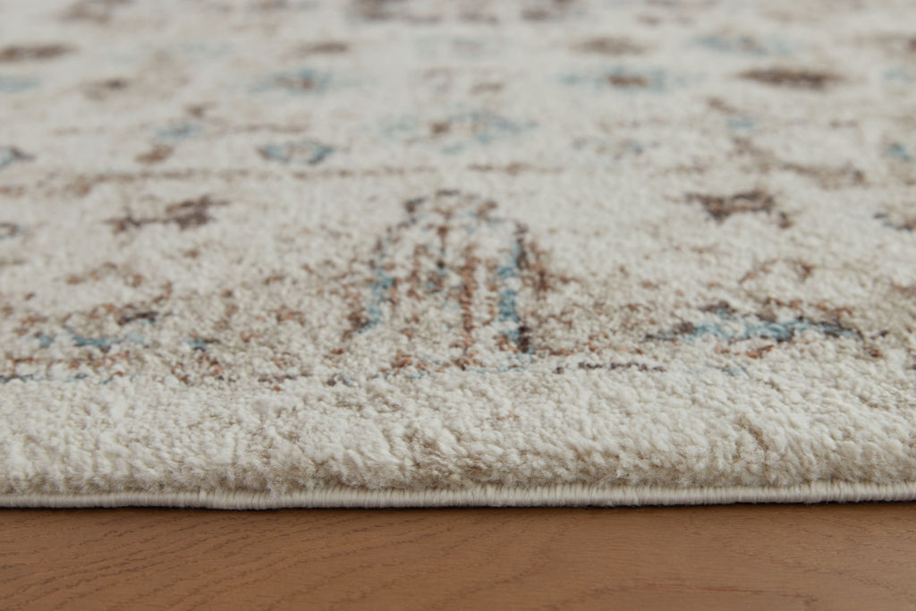 Beige area rug surface with distressed motif details in brown and blue-green