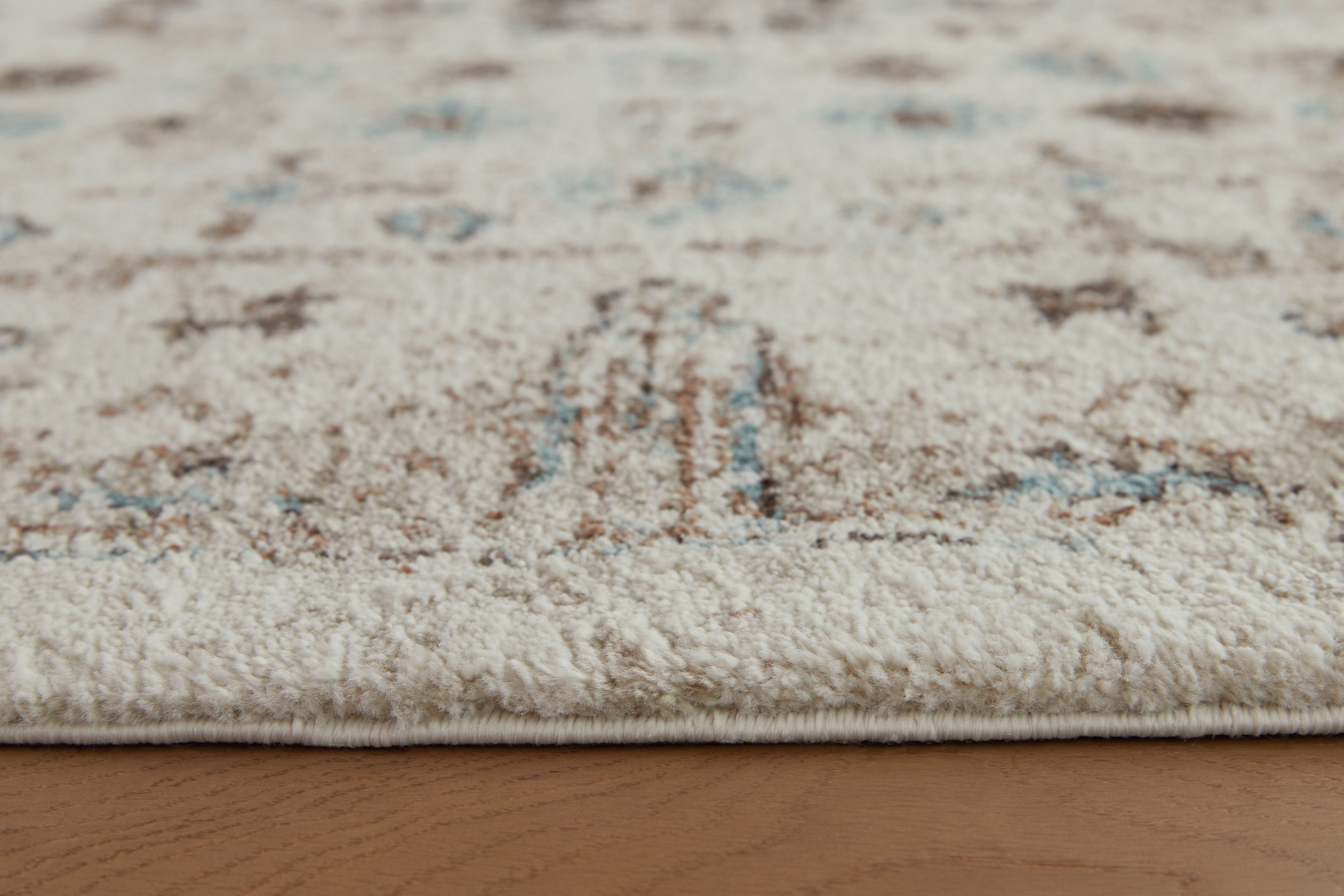 Beige area rug surface with distressed motif details in brown and blue-green