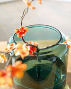 Teal glass vase holding orange blossoms on dark branches
