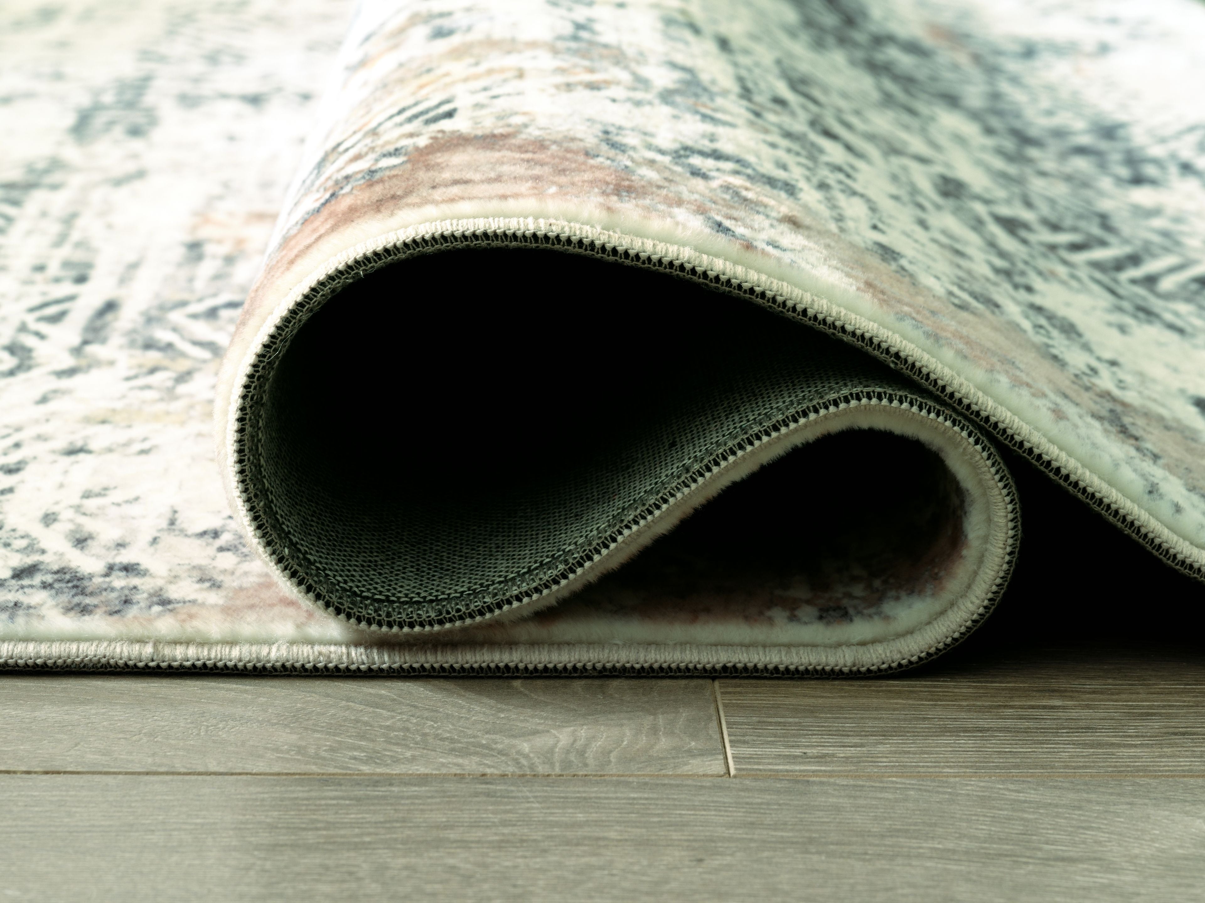 Area rug edge close-up with dark backing and rolled border