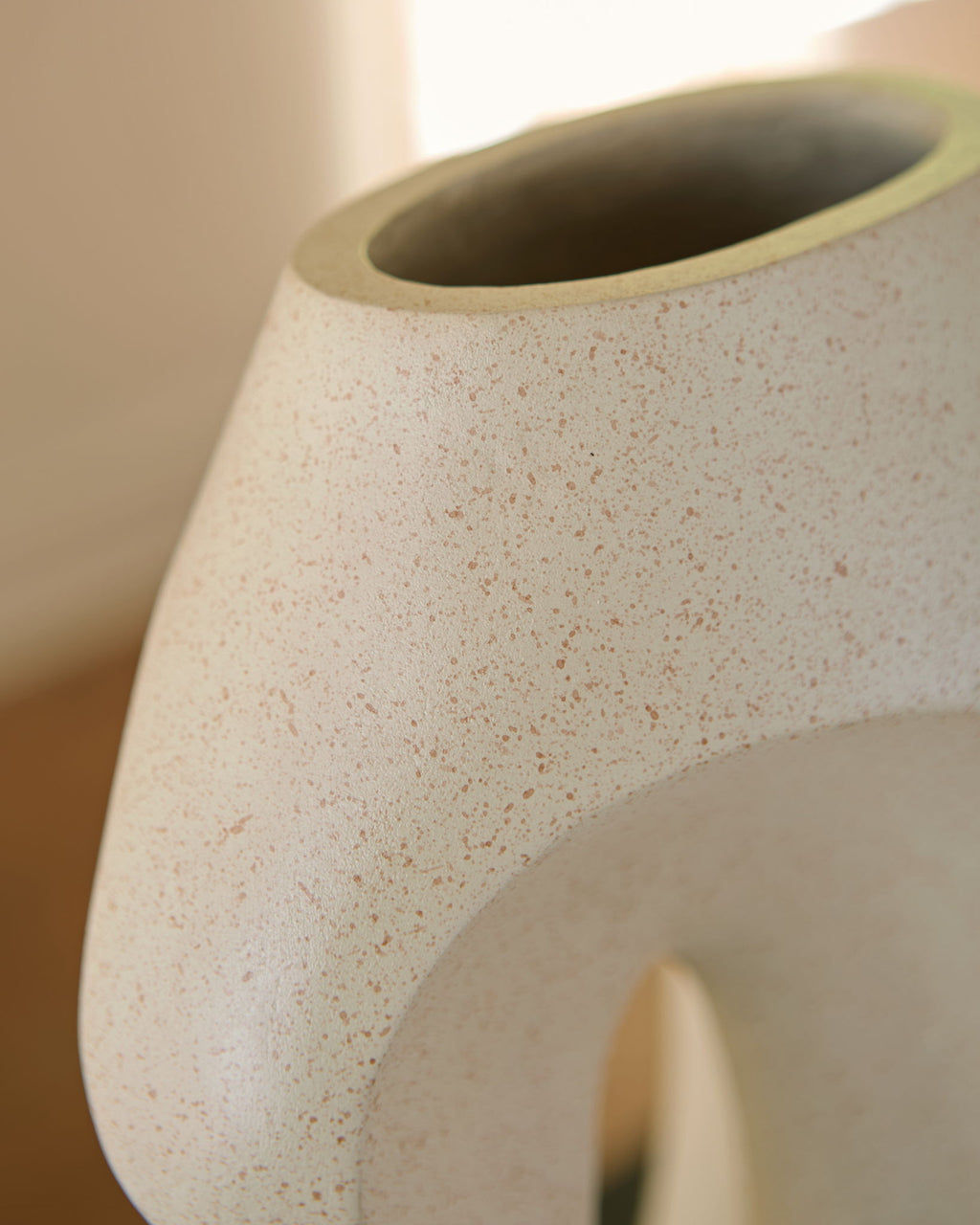 Beige ceramic vase close-up showing speckled texture and side cutout.