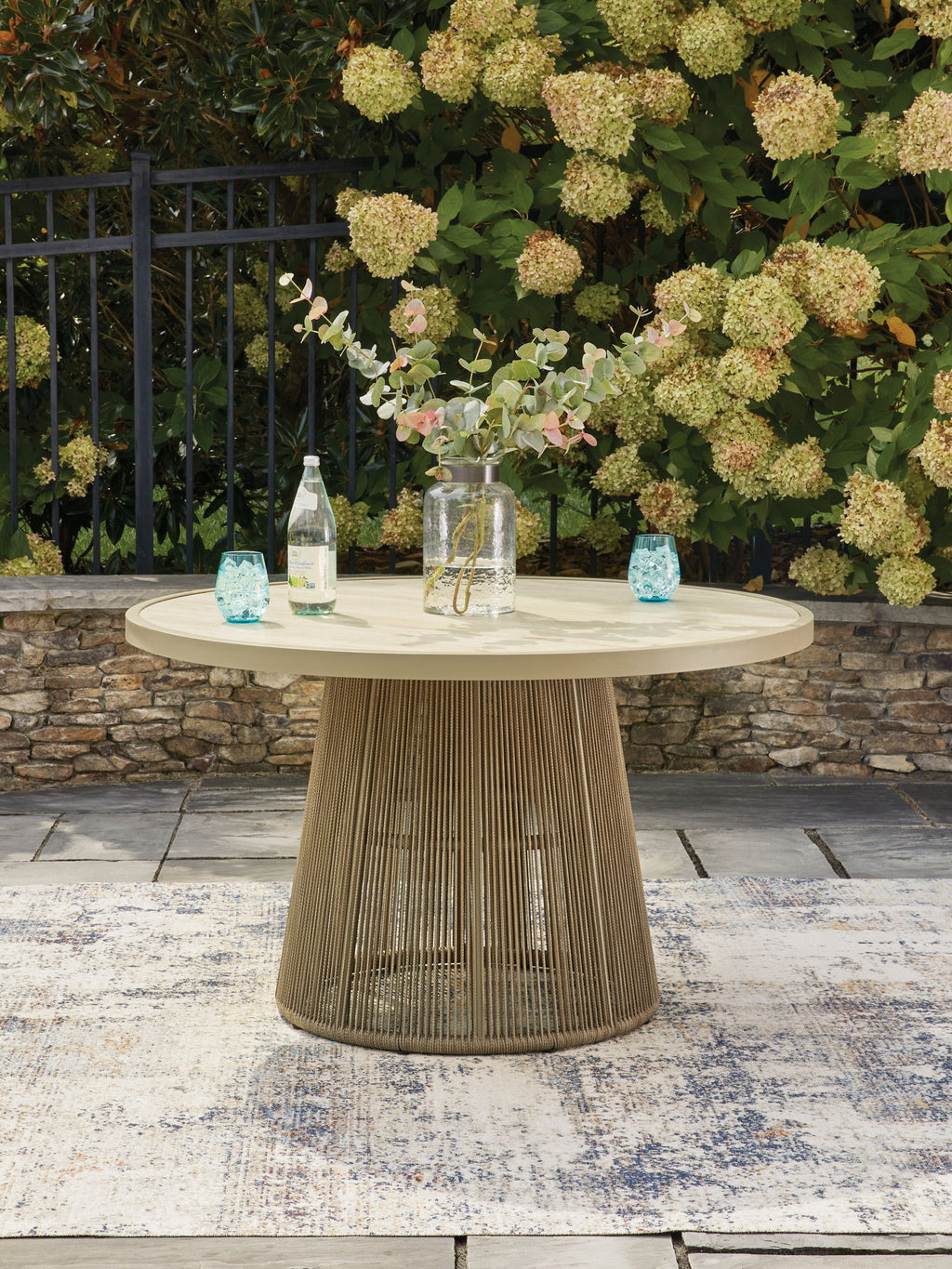 Beige outdoor dining table with round tabletop and woven pedestal base