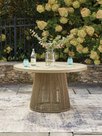Beige outdoor dining table with round tabletop and woven pedestal base