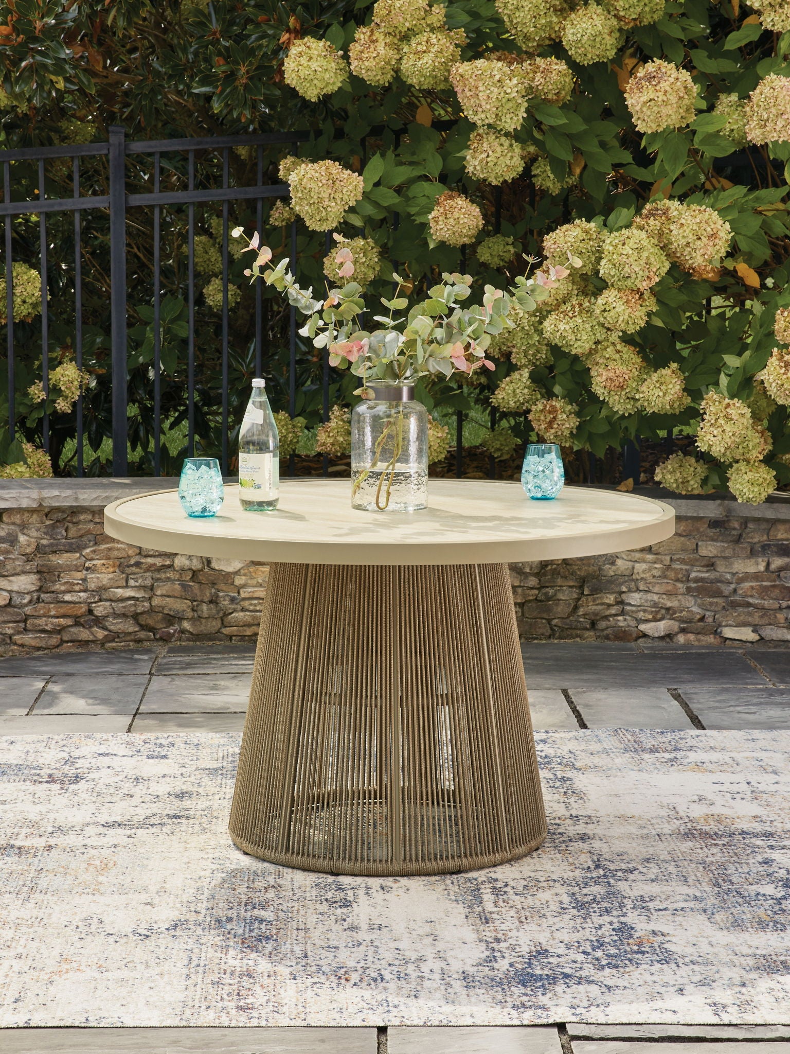 Beige outdoor dining table with round tabletop and woven pedestal base