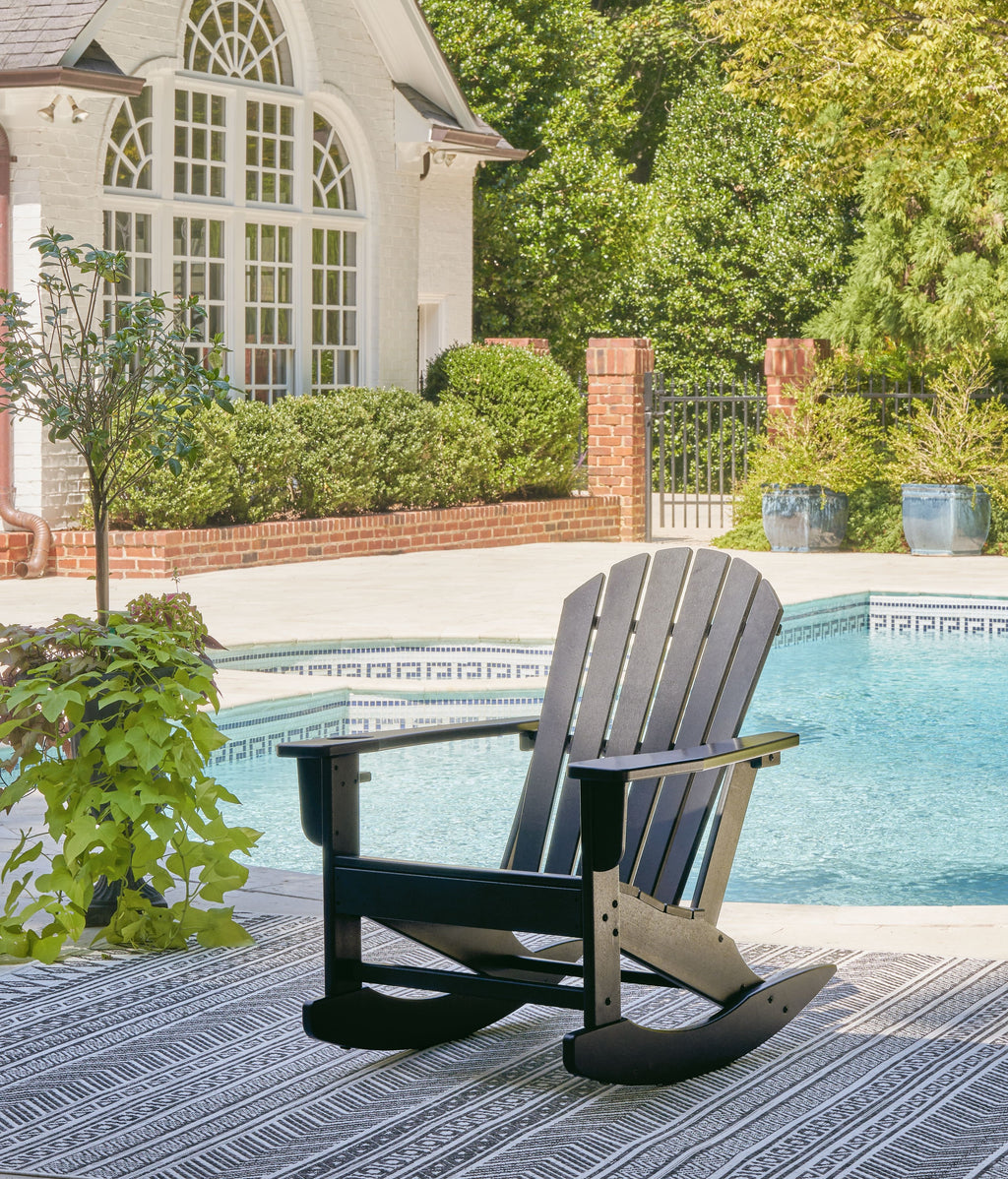 Dark gray Adirondack rocking chair with slatted back and armrests on outdoor deck.
