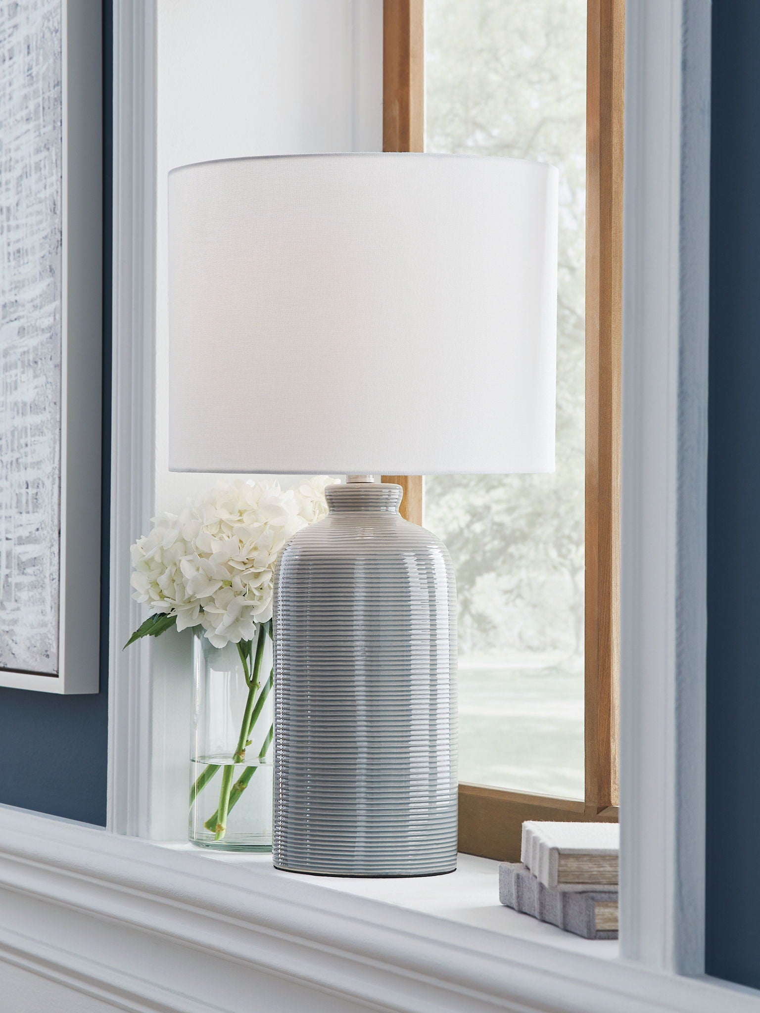 Gray blue ribbed ceramic table lamp with white drum shade on tabletop