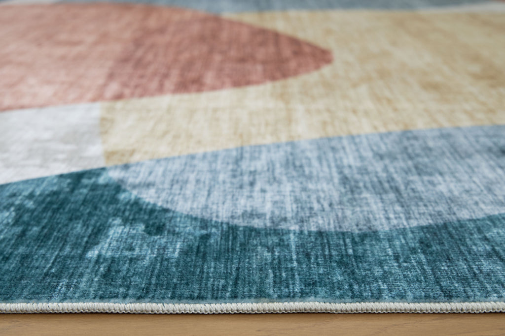 Blue washable rug with abstract geometric blocks in beige, coral, and light gray