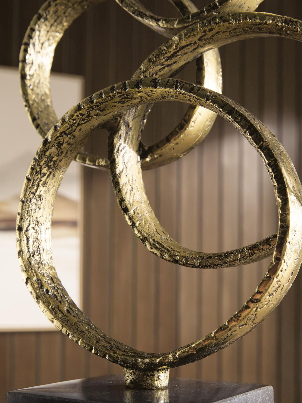 Close-up of gold-finish textured metal rings over a dark pedestal base