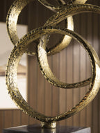 Close-up of gold-finish textured metal rings over a dark pedestal base