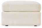Cream accent ottoman with cushioned top and square base, low dark legs.